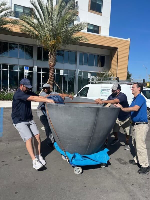 Four Firehawk installers moving an 1,800-pound concrete planter on a dolly at The Maxwell at Xentury City