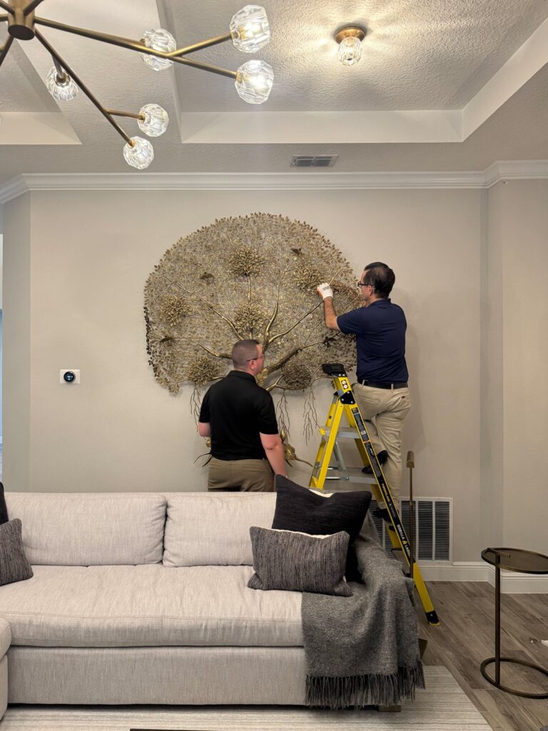 Firehawk installers Sydney and Robert hanging a large metal tree sculpture over a sofa